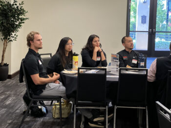 Four students listening to speaker at podium