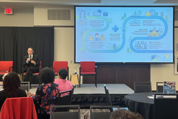 Speaker on stage with PowerPoint over his shoulder