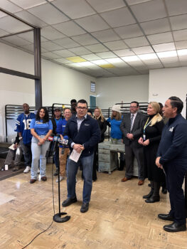 Nick Macchione stands at a microphone with people behind him