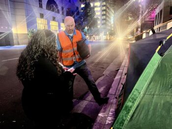 Two homeless outreach workers, one wearing an orange vest engage with someone inside a tent during the 2025 point in time count
