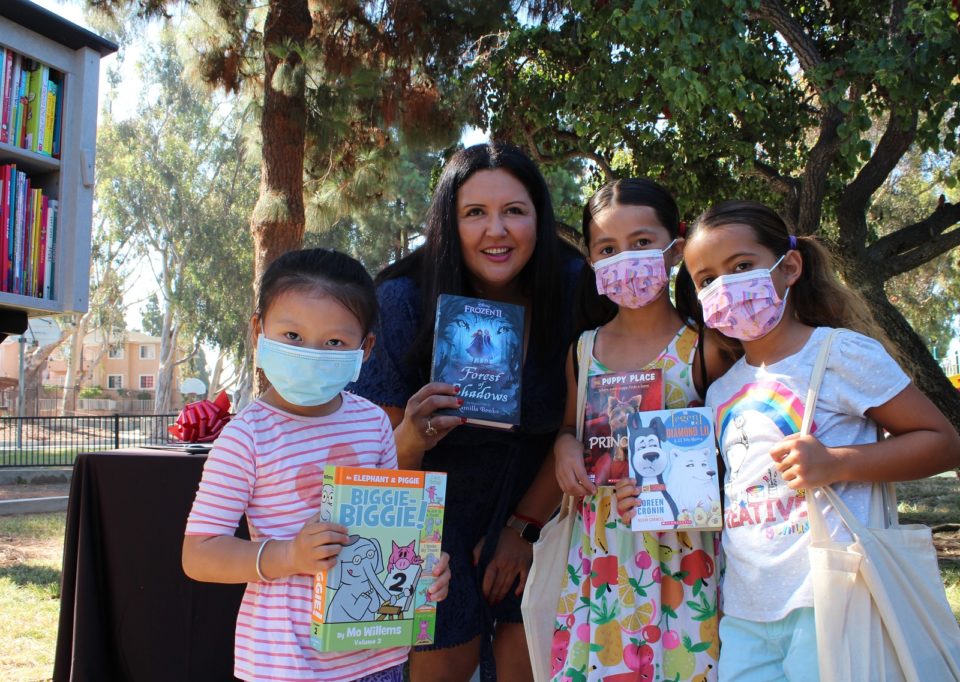 Nora Varas with three girls in front of a Little Free Library
