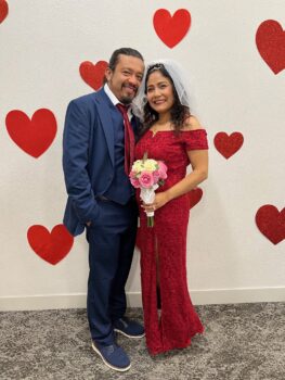 Couple stands close together in front of wall with hearts
