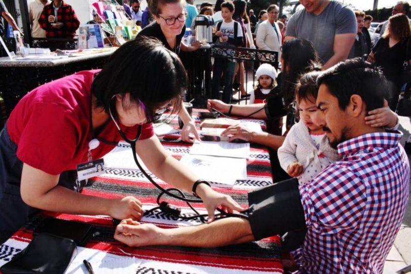Man sits with child in lap while getting blood pressure checked