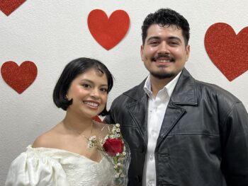 Couple stands in front of heart wall