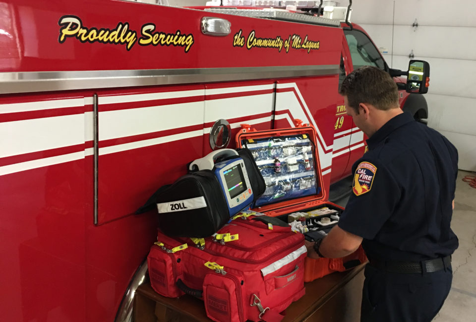 Firefighter Paramedic checking advanced lifesaving equipment next to a fire truck.