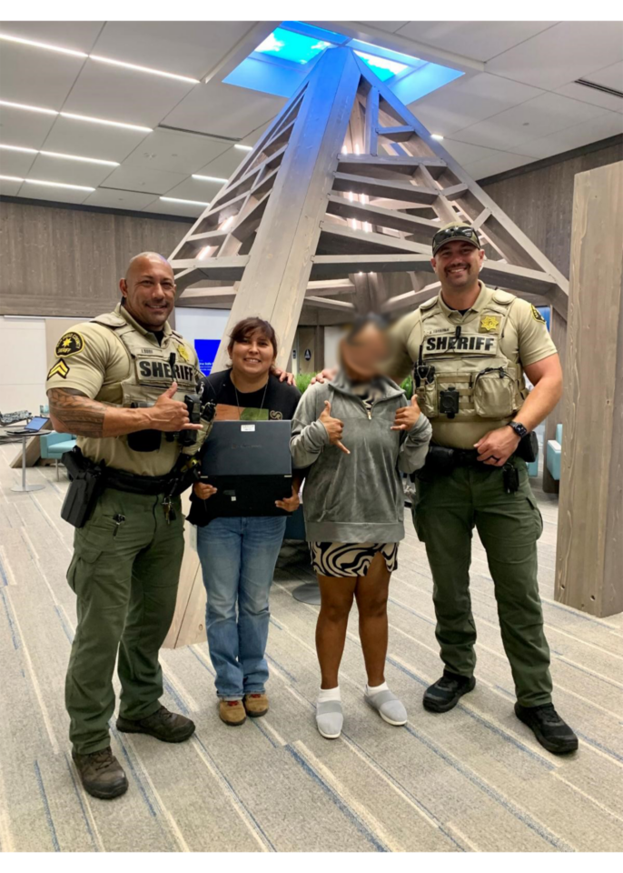 Four people standing in the lobby of One Safe Place. They are in a line with Deputies posing on each end and two women in the middle. All are smiling.