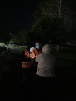 2 volunteers in orange vests speak to a person wearing a sweatshirt