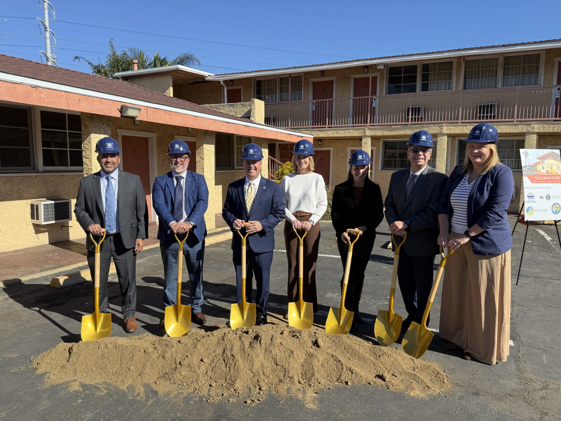 Group with shovels in dirt in front of a motel