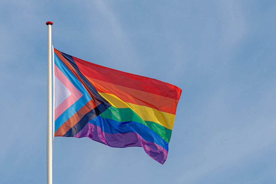 Pride Progress flag flies in blue sky