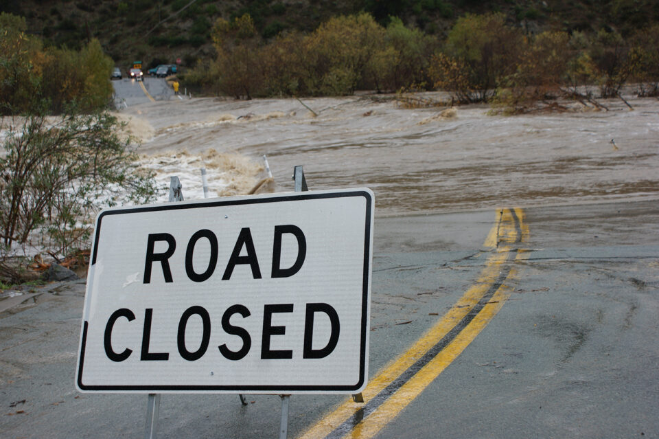 Picture of County Road with water running across it and a Road Closed sign blocking it
