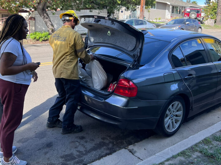 people loading sandbags into the trunk of a car