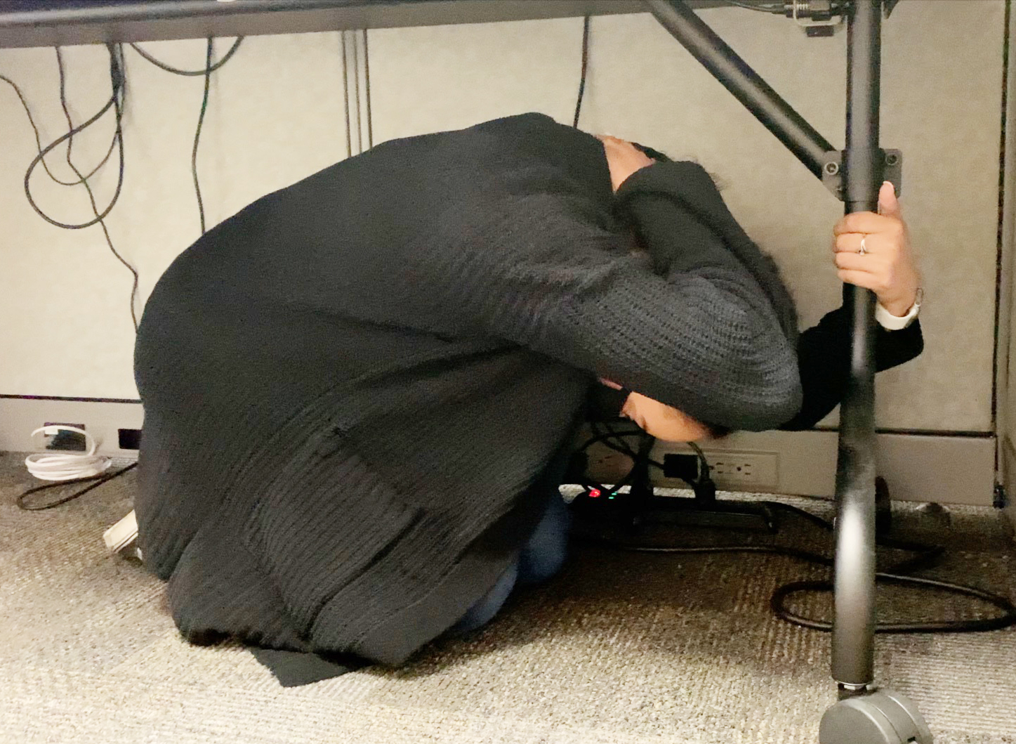 Employee under a desk covering head for earthquake drill.