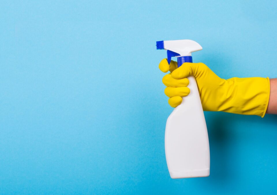 hand wearing glove holds cleaning bottle with spray nozzle