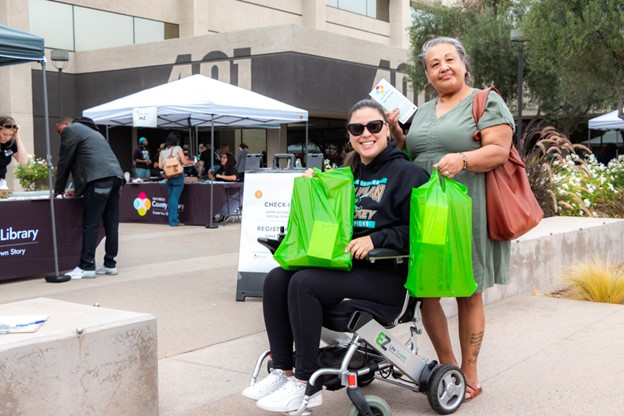 Two women in front of the County Library holding new laptops. One woman is in a wheelchair.