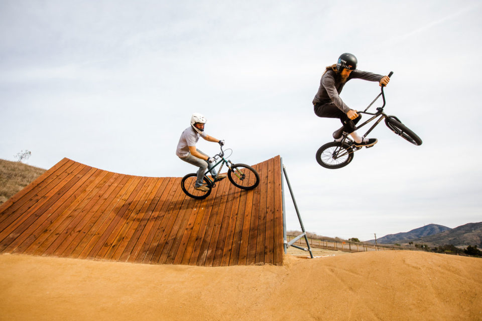 Two mountain bike riders on a jump track. One catching air.