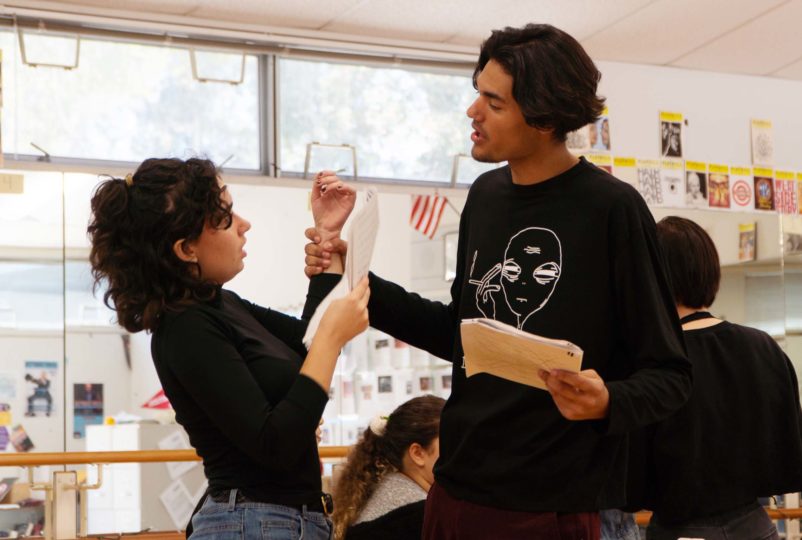 A teenage actor grabs a teenage actress' wrist in a threatening manner while practicing a scene from a play about human trafficking.