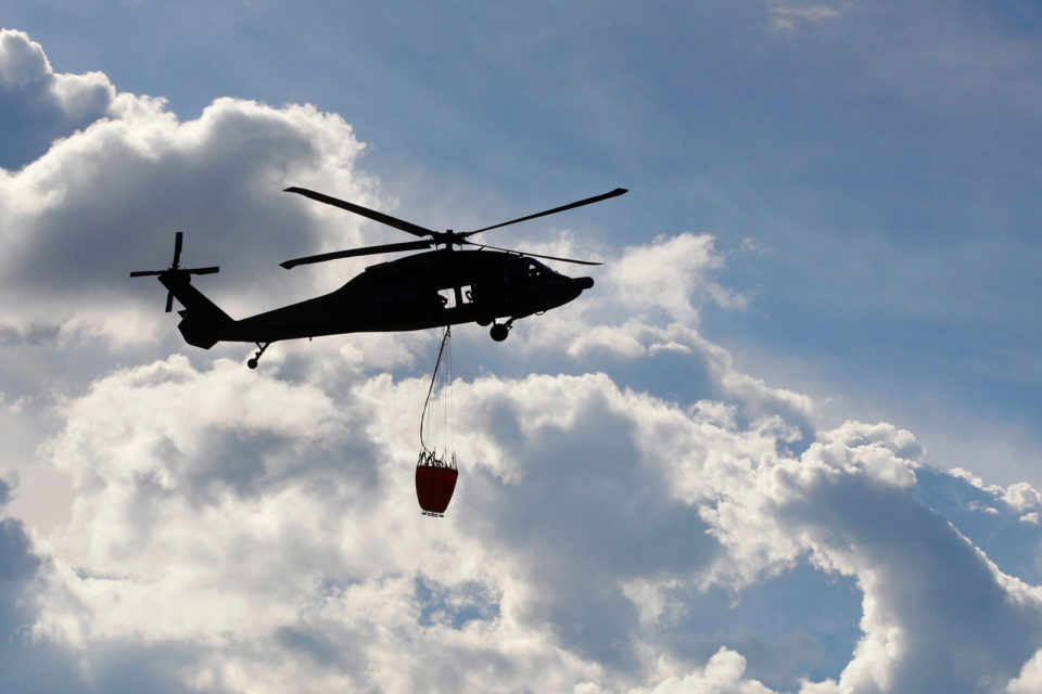 Stock photo of a UH-60 Black Hawk helitanker in the air hoisting a water bucket.