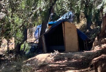 makeshift tent home in rural area with tarps as the roof and a dirt floor.
