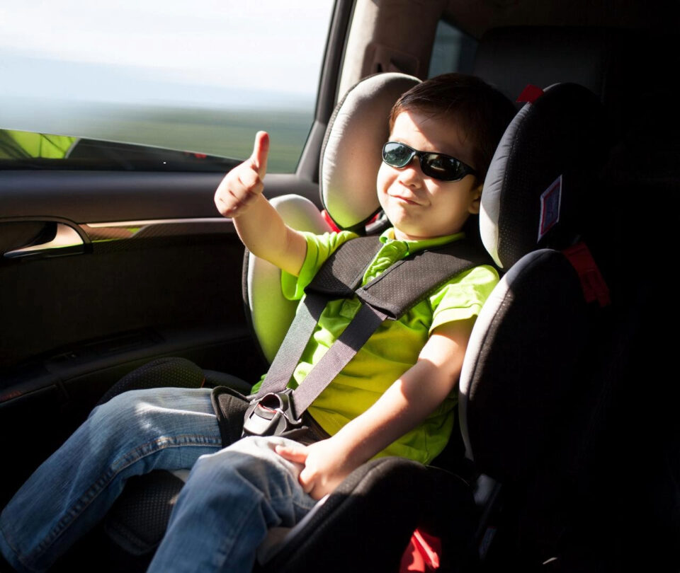 Boy in car seat with sunglasses giving a thumbs up
