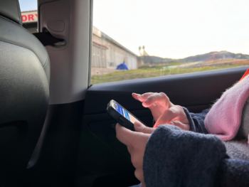 a person enters information into a cellphone from the backseat of a car