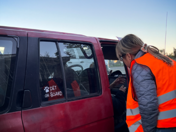 a volunteer wearing a vest speaks to a person in the passenger seat of a vehicle