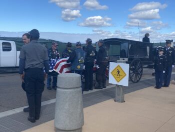 Patriot Guard carries flag covered casket while men and women in uniform salute