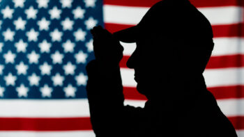 silhoutte of vetearn saluting in front of flag