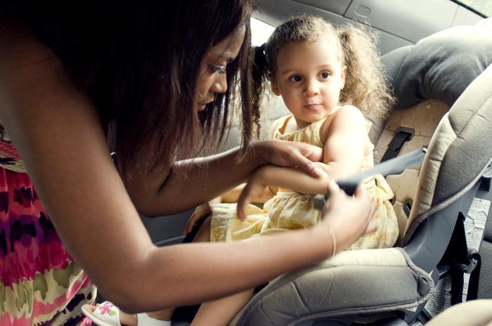 a mother in the process of securing her young daughter into her child safety seat, located in the vehicle’s rear seat. At this point in the process, she was adjusting her daughter’s harness, ensuring both her safety and comfort.