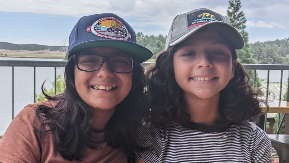 two children smile in front of lake