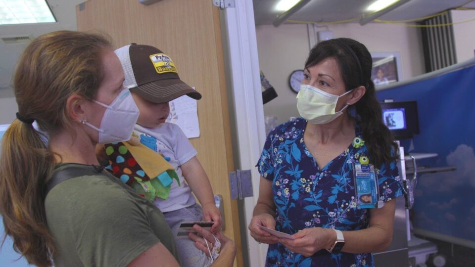 woman holds child and stands with medical professional