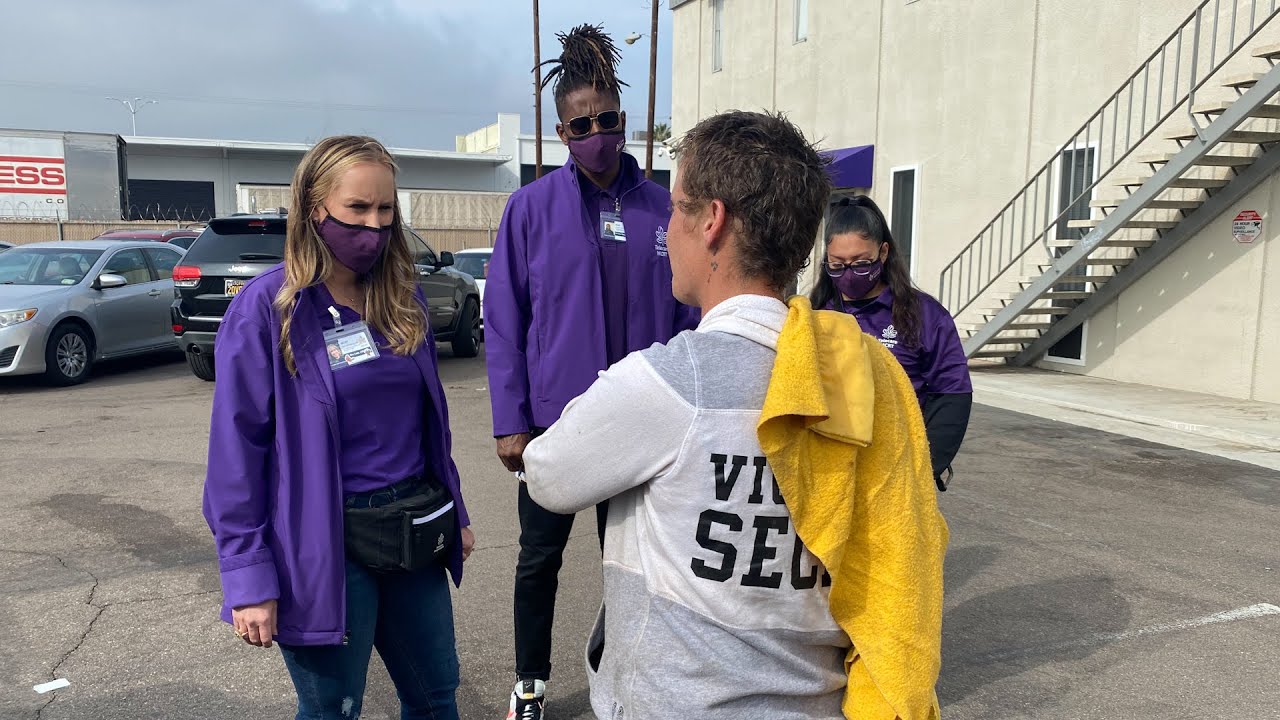 3 people in purple speak to someone in a parking lot