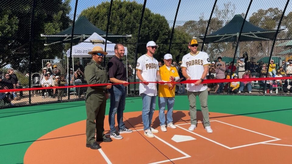 People stand near home plate cutting a large ribbon