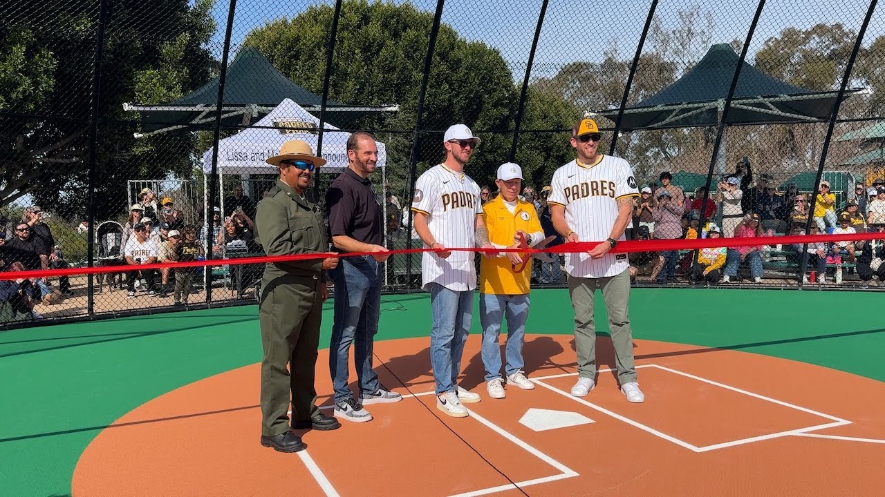 People stand near home plate cutting a large ribbon