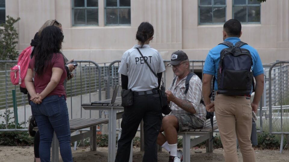 a team of people assisting a man sitting at a picnic table