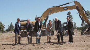 officials hold shovels in front of construction equipment