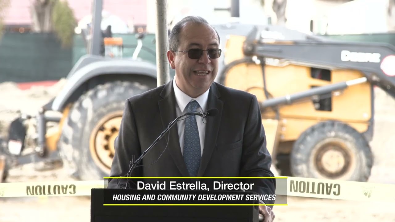 David Estrella stands at a podium in front of construction equipment