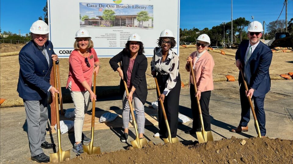 6 people wearing hard hats hold shovels in dirt