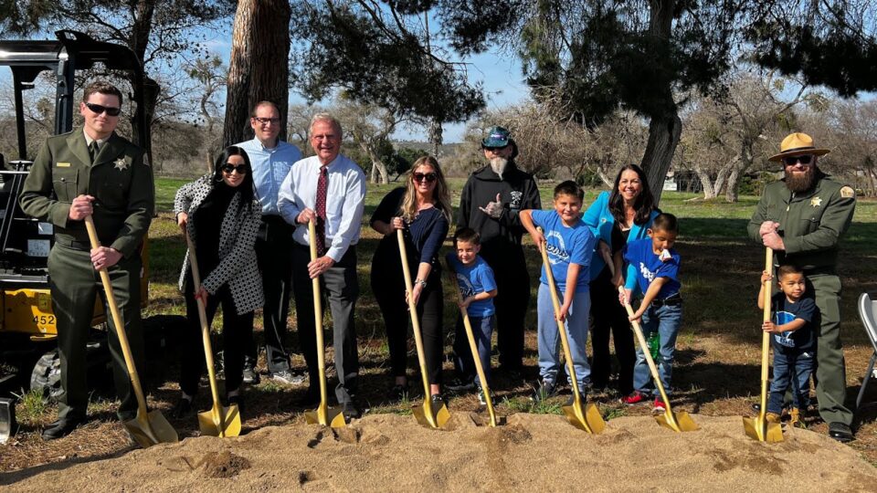 many people of different ages hold shovels in dirt at park