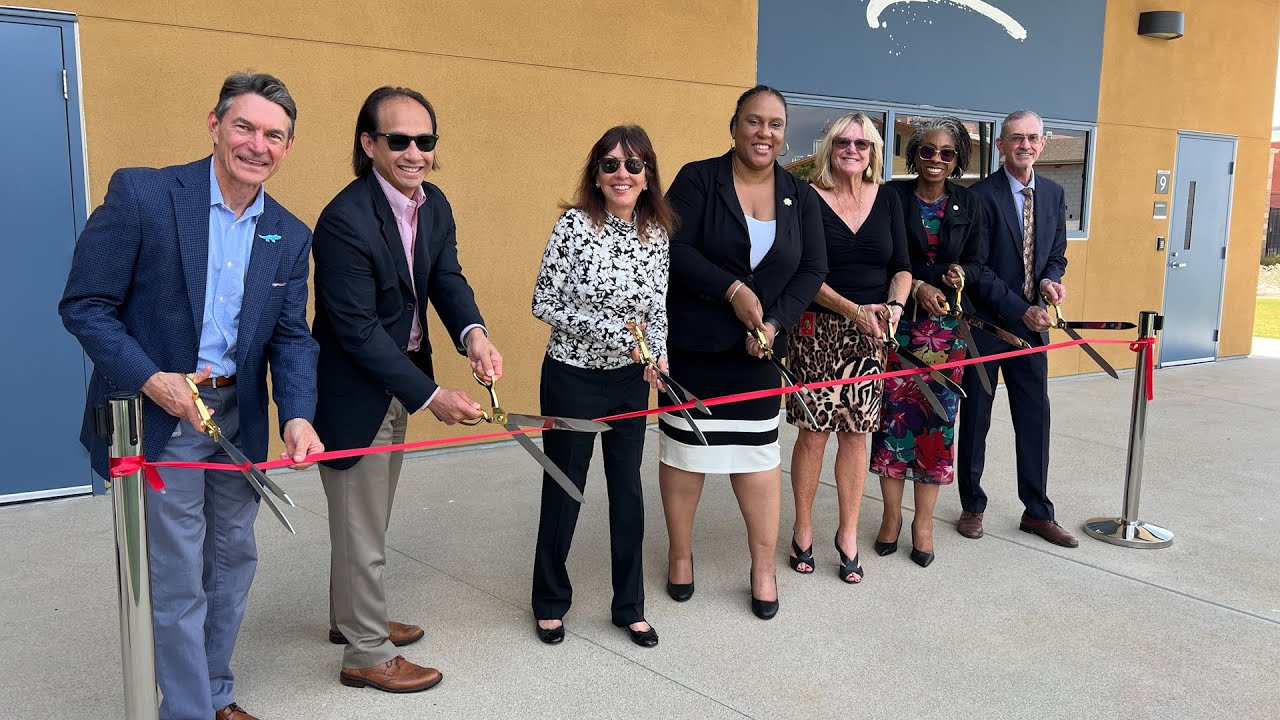 group of people cut red ribbon in front of building