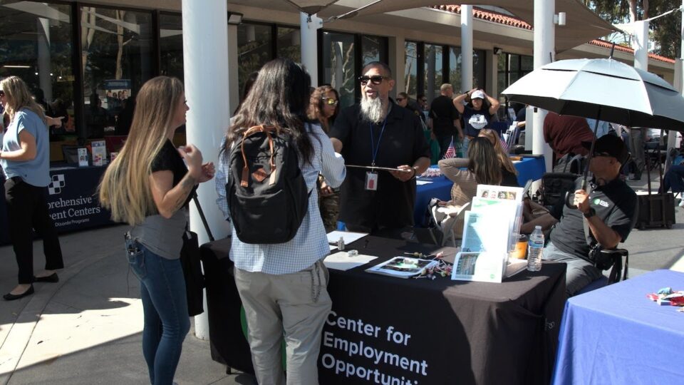 two people speak to someone at an info table
