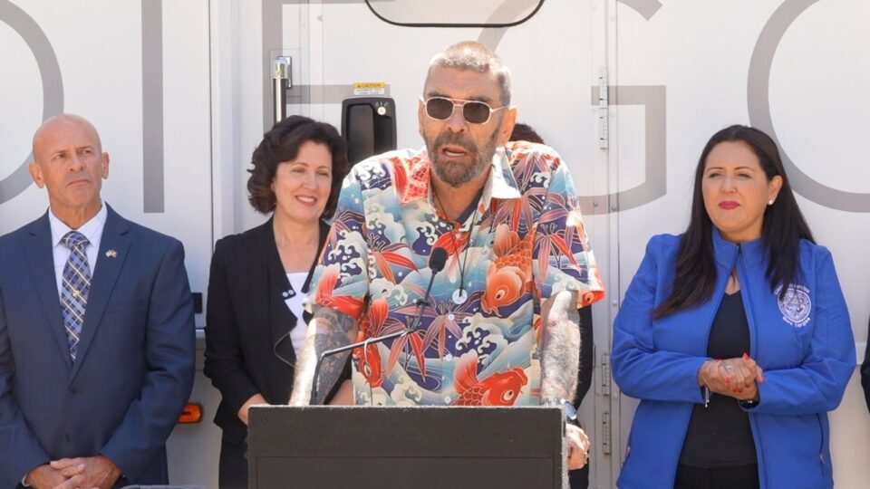 man stands at podium with people behind him