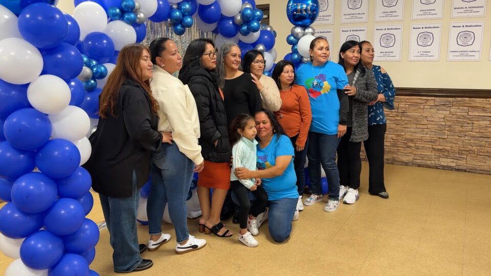 big group of people stand in front of blue and white balloon arch