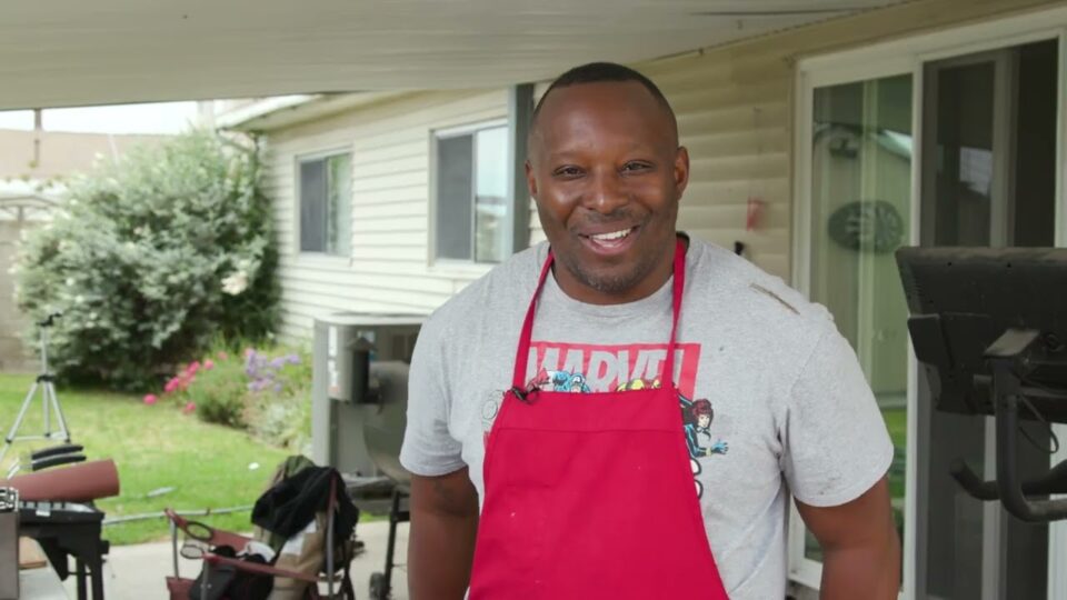 man with apron stands in backyard
