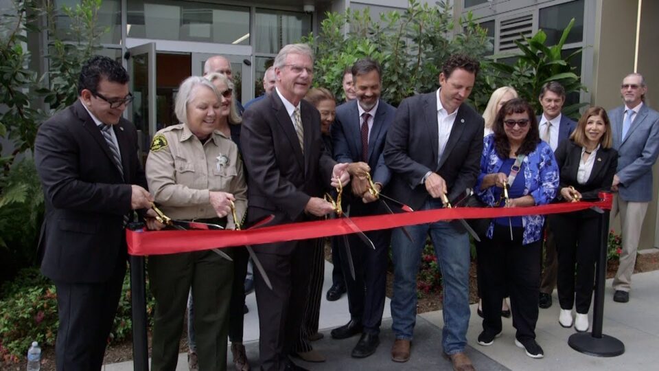 official cut a large red ribbon in front of a building