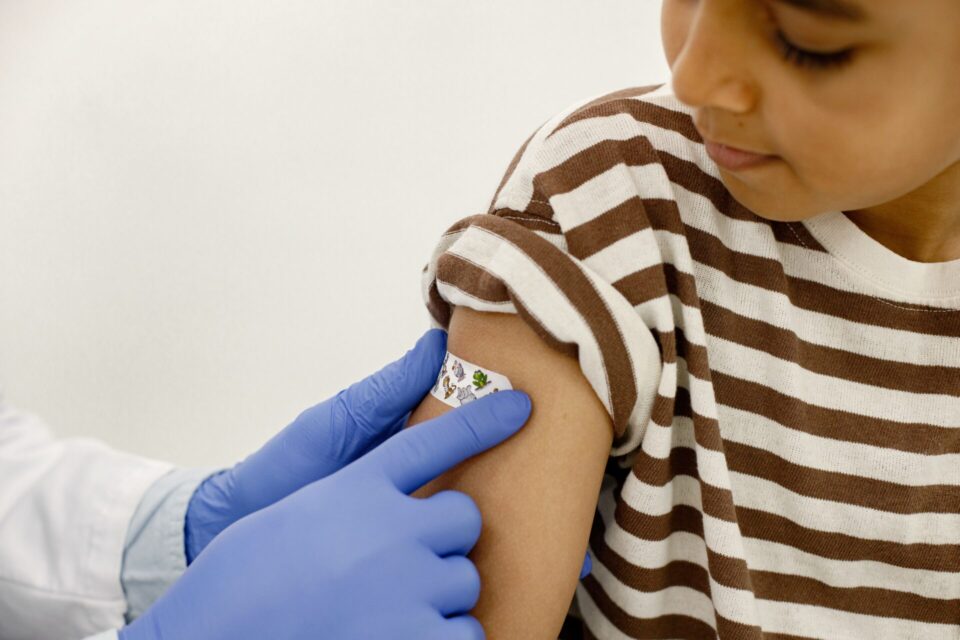 Child in striped shirt getting band aid placed on arm