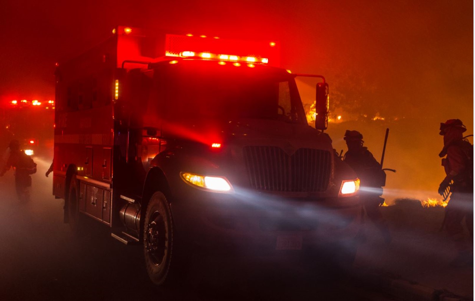 Fire engine at night with lights on and red glow behind.