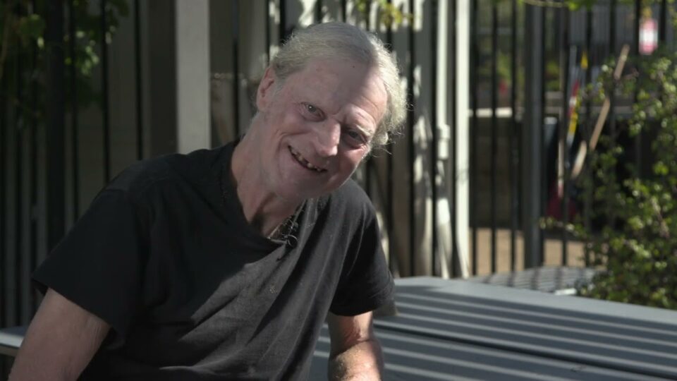 man smiles outside house