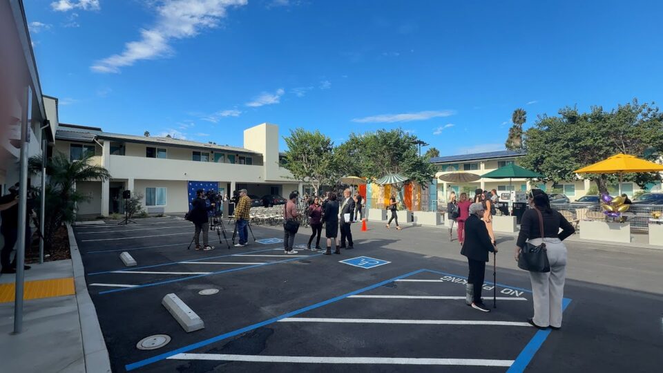 people stand around a parking lot outside a two-story building