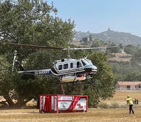 Sheriff's helicopter equipped for firefighting lowering the snorkel into a HeloPod tank to refill with water