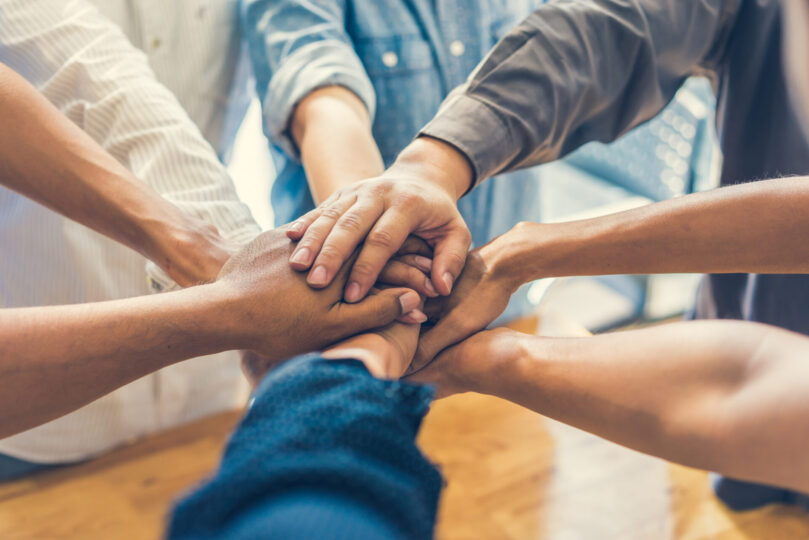 people huddle together overlapping hands